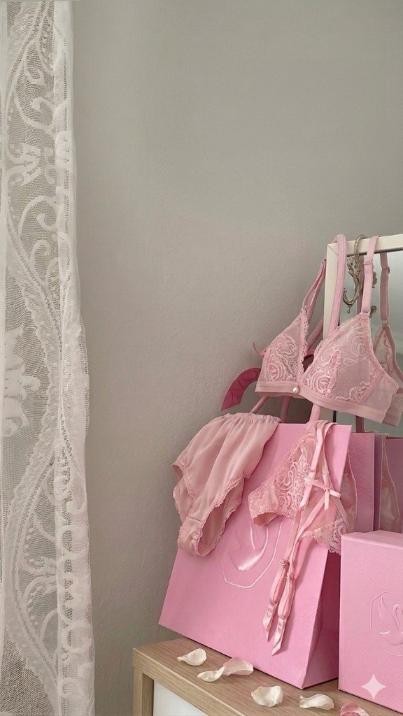 Pink lace lingerie set displayed on a hanger with rose petals and gift bags